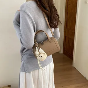 Close-up detail of stylish brown pillow bag with cute plush bear pendant, fashion commuter crossbody.