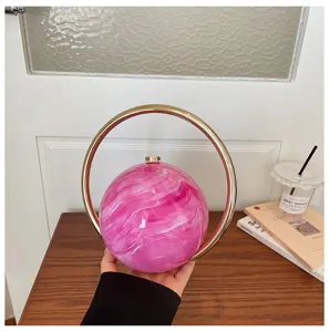 Close-up of pink marble round handbag with gold metal ring handle, elegant evening clutch.