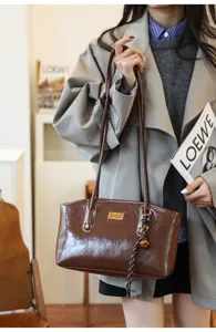 Brown PU shoulder bag detail shot, featuring metal plaque and chic charm pendant.