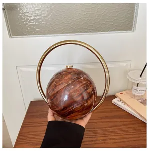 Spherical clutch bag with large metal ring handle, chic amber resin design, elegant detail shot.