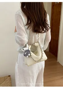 Elegante cremeweiße Schultertasche im Detail mit grober Kette und süßem Plüschanhänger.