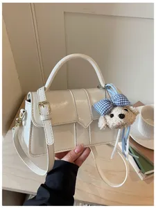 Nahaufnahme der weißen Leder-Umhängetasche mit süßem Teddybär-Anhänger und Goldbeschlägen.