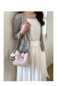 Nahaufnahme einer rosa Leder Schultertasche mit Metallverschluss und süßem Plüschanhänger im Alltag.