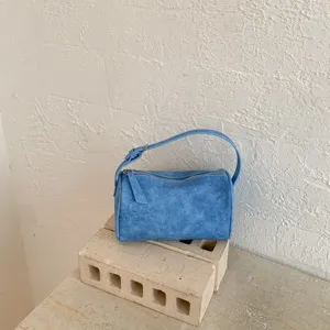 Detalle de textura de ante azul del bolso de mano tipo almohada minimalista con cremallera.