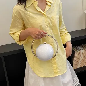 Detail shot of a unique spherical handbag with gold ring handle and elegant chic outfit.