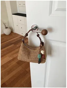 Detailansicht einer gewebten Stroh-Umhängetasche an einer Türklinke mit bunten Perlenanhängern.