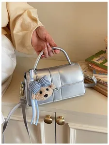 Silberne metallische Umhängetasche mit süßem Bärenanhänger, schicke Pendler-Taschendetails.