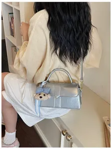 Detailaufnahme einer schicken silbernen Umhängetasche mit süßem Bärenanhänger für Damen.
