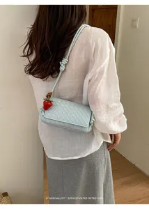 Detail view of light blue woven leather shoulder bag with cute strawberry charm and knot strap.