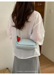Close-up detail of light blue woven leather shoulder bag with cute strawberry charm style.