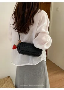 Detail view of stylish black woven leather crossbody bag with cute strawberry charm.