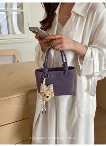 Lila Eimer-Tasche Detail mit eleganten Henkeln und einem süßen Bären-Anhänger.