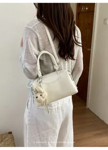 Detailaufnahme einer eleganten weißen Boston Handtasche mit süßem Plüsch Bär Anhänger.