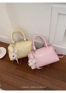Detailaufnahme trendiger PU Boston Handtaschen in Gelb und Rosa mit süßen Plüsch-Hundeanhängern.