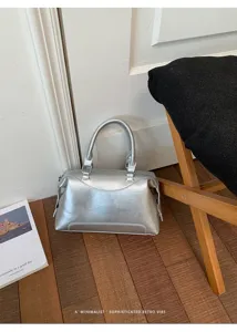 Silberne Boston Handtasche Detailansicht mit Metallic-Textur, doppelten Griffen und Design.
