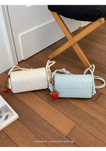Detailed view of chic woven leather crossbody bag with cute strawberry pendant accessory.