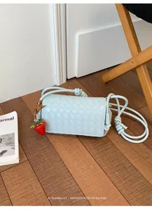 Light blue woven leather crossbody bag with chic knot handle and cute strawberry charm.