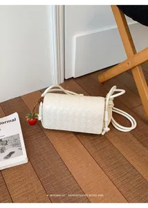Detail shot of white woven leather crossbody bag with knot strap and cute strawberry charm.