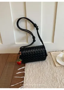 Black woven leather shoulder bag detail, elegant knotted strap and charming strawberry pendant.