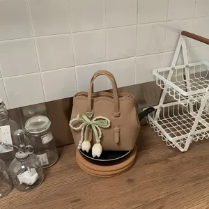 Beige Leder Eimer Tasche Detail mit Perlen Schleife und Tulpen Anhänger auf Küchentheke.