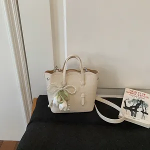 Beige Leder-Eimerhandtasche Detail mit gewelltem Rand, Griffen und schickem Perlen-Tulpen-Anhänger.
