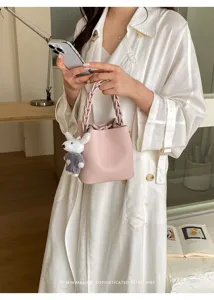 Modische rosa Leder Eimer Tasche für Damen mit geflochtenem Griff und süßem Anhänger.