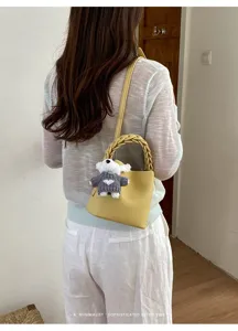 Detailansicht der gelben Beuteltasche mit geflochtenem Griff und süßem Bären-Anhänger.