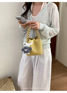 Detailansicht einer stilvollen gelben Leder-Eimer Tasche mit geflochtenem Henkel und Bär.