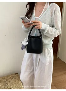 Schicke schwarze Leder-Eimer Tasche mit geflochtenem Griff und süßem Kaninchen-Anhänger Sommer.