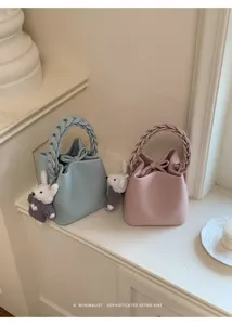 Detailansicht trendiger Damen Eimer Umhängetaschen mit geflochtenem Griff und Anhänger.