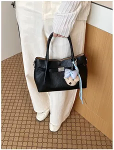 Detalle de bolso tote de cuero negro con cierre de vuelta de metal y colgante de lazo de felpa.