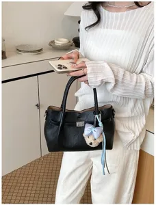 Elegante bolso tote negro con correa, cierre de metal y colgante de osito adorable.