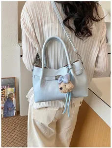 Vista detallada del bolso de hombro azul claro para mujer con dije de oso y cierre elegante.