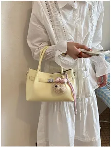 Vista detallada de un elegante bolso amarillo claro con colgante de osito y cerradura.