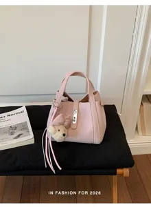 Vista de detalle del elegante bolso de cubo de cuero rosa con bonito colgante de oso de peluche.