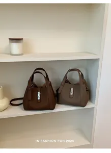 Vista detallada del elegante bolso cubo marrón con cierre de metal en estante limpio.