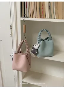 Minimalistische Damen Beuteltasche mit geflochtenem Griff und süßem Plüschhasenanhänger.