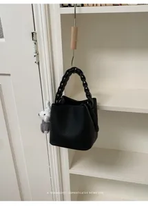 Schwarzes Leder Eimer Tasche Detail mit geflochtenem Griff und süßem Plüsch Anhänger Zubehör.