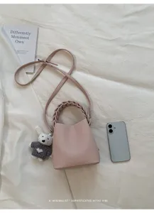 Rosa Leder-Eimer-Taschen-Detail mit geflochtenem Griff und Bärenanhänger auf weißem Stoff.