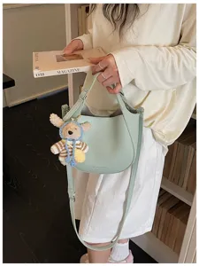 Sac seau élégant en cuir vert avec bandoulière et charm d'ours mignon pour style quotidien.