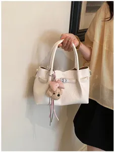 Elegante bolso de mano crema para mujer con dije de oso y cierre de giro elegante.