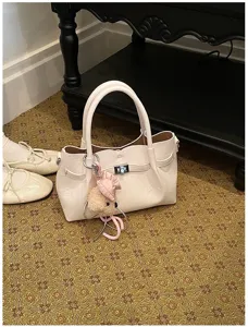 Elegante bolso de mano en color crema con cierre de giro y tierno colgante de felpa.