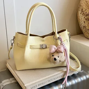 Elegante bolso de hombro tote amarillo para mujer con colgante osito de peluche y cierre.