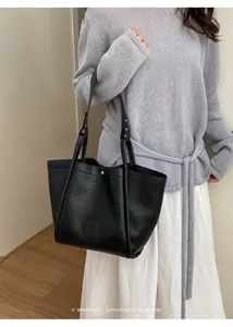 Gros plan sur le sac seau fourre-tout en cuir noir porté à l'épaule, look rétro minimaliste.
