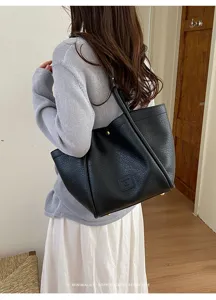 Vue détaillée du sac cabas en cuir texturé noir au design minimaliste et aux pieds métalliques.