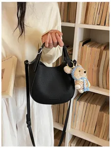 Sac seau en cuir noir avec poignée, bandoulière et adorable pendentif ours en peluche.