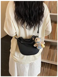 Vue détaillée d'un élégant sac à bandoulière en cuir noir avec un charm ours en tricot.