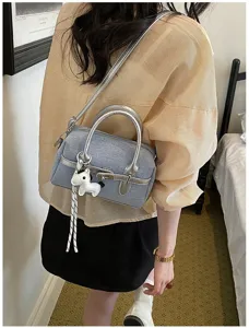 Detailed view of the stylish contrast color shoulder pillow bag with silver handle and cute charm.