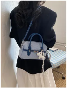 Detailed shot of the blue denim contrast shoulder bag featuring twin handles and a cute dog charm.