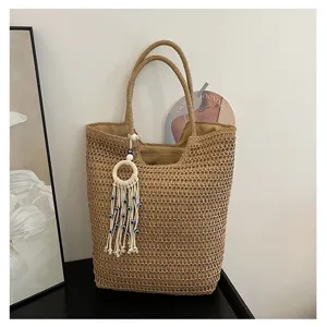 Detailansicht der Strohtasche mit Struktur und schickem Anhänger vor hellem Hintergrund.